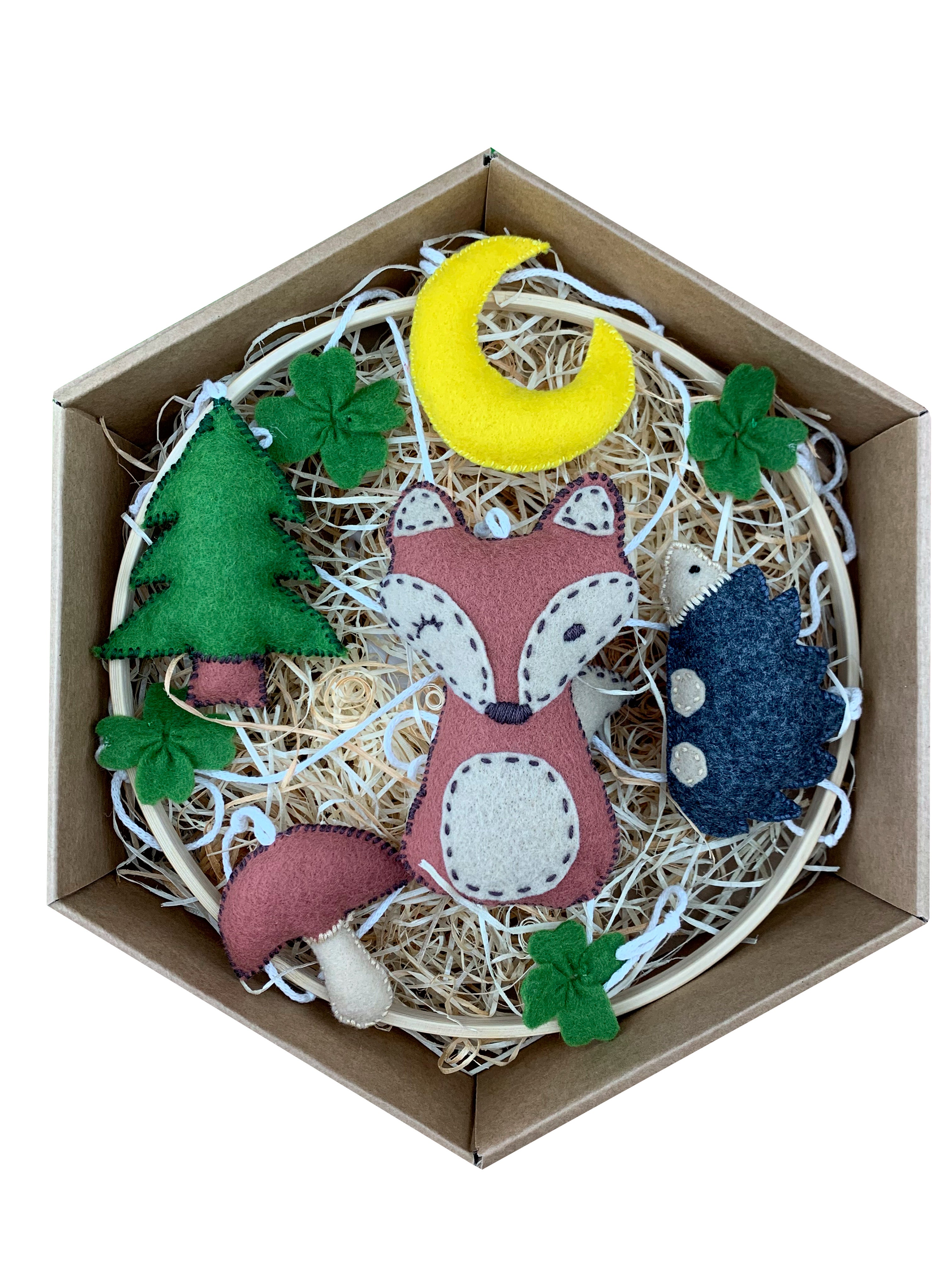 Dárkové balení dětského závěsného kolotoče s lesními motivy. Uvnitř krabičky na podestýlce z dřevité vlny jsou ručně šité filcové dekorace: liška, ježek, smrkový strom, měsíček, houba a několik zelených lístků.