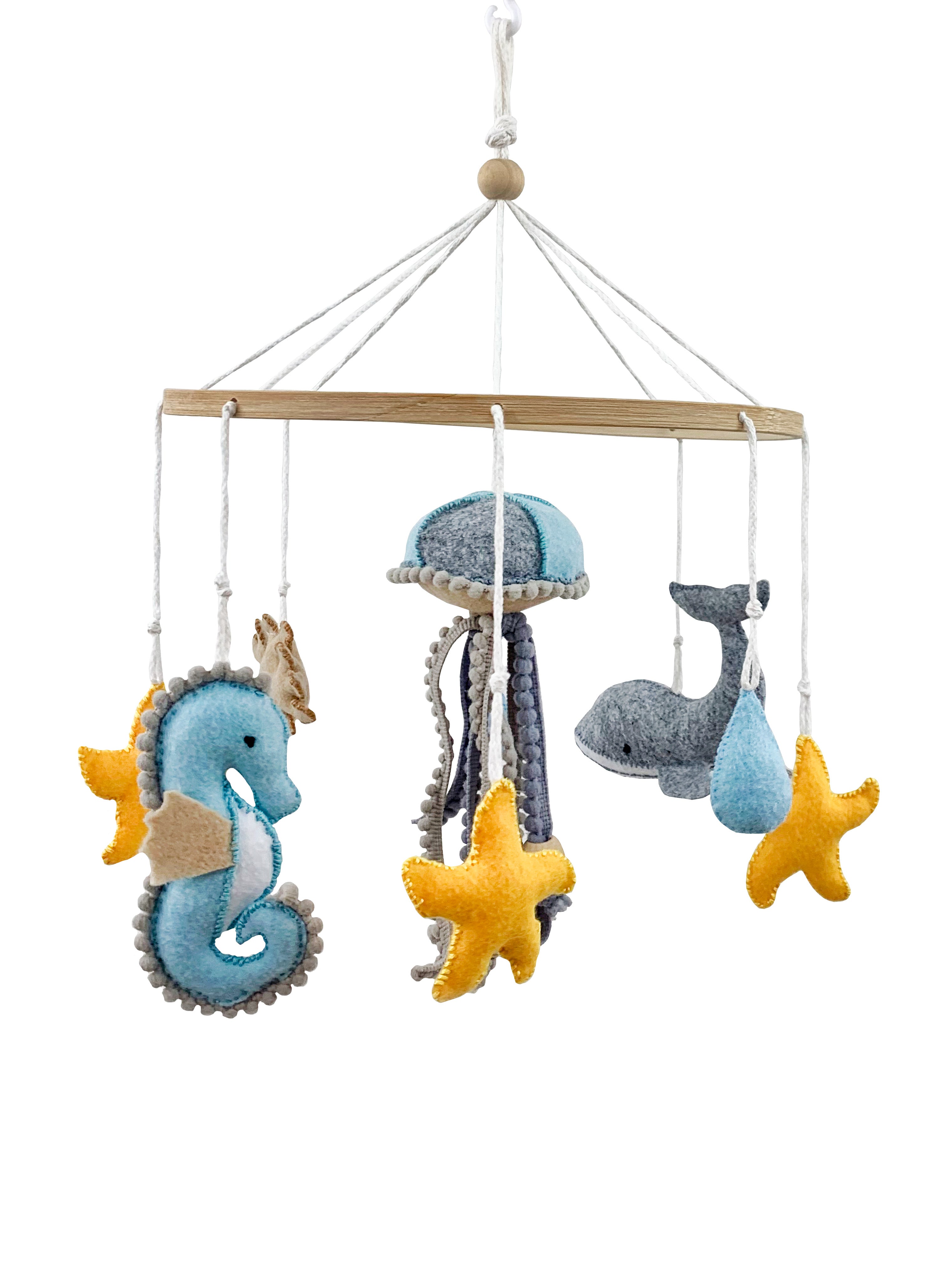 Závěsný dětský kolotoč s mořskými motivy. Na dřevěném kruhu visí ručně šité filcové dekorace: mořský koník, medúza s dlouhými chapadly, velryba, kapka vody a žluté hvězdice. Celý kolotoč je zavěšený na bílých šňůrách s dřevěnou kuličkou uprostřed.