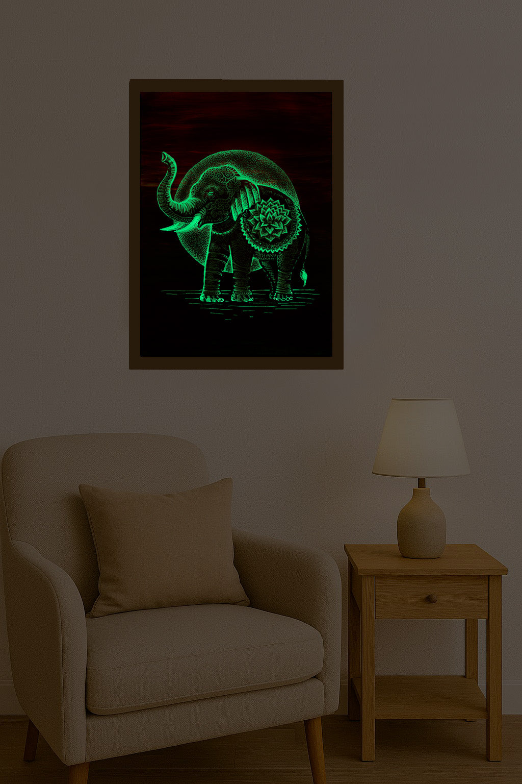 Svítící autorský obraz slona s mandalovým zdobením, který ve tmě září zeleným glow efektem, zavěšený nad křeslem a stolkem s lampou v tlumeném interiéru.
